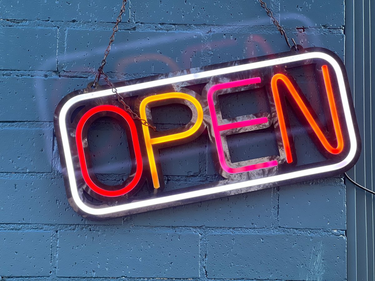 Colourful neon open sign on a small business blue brick wall