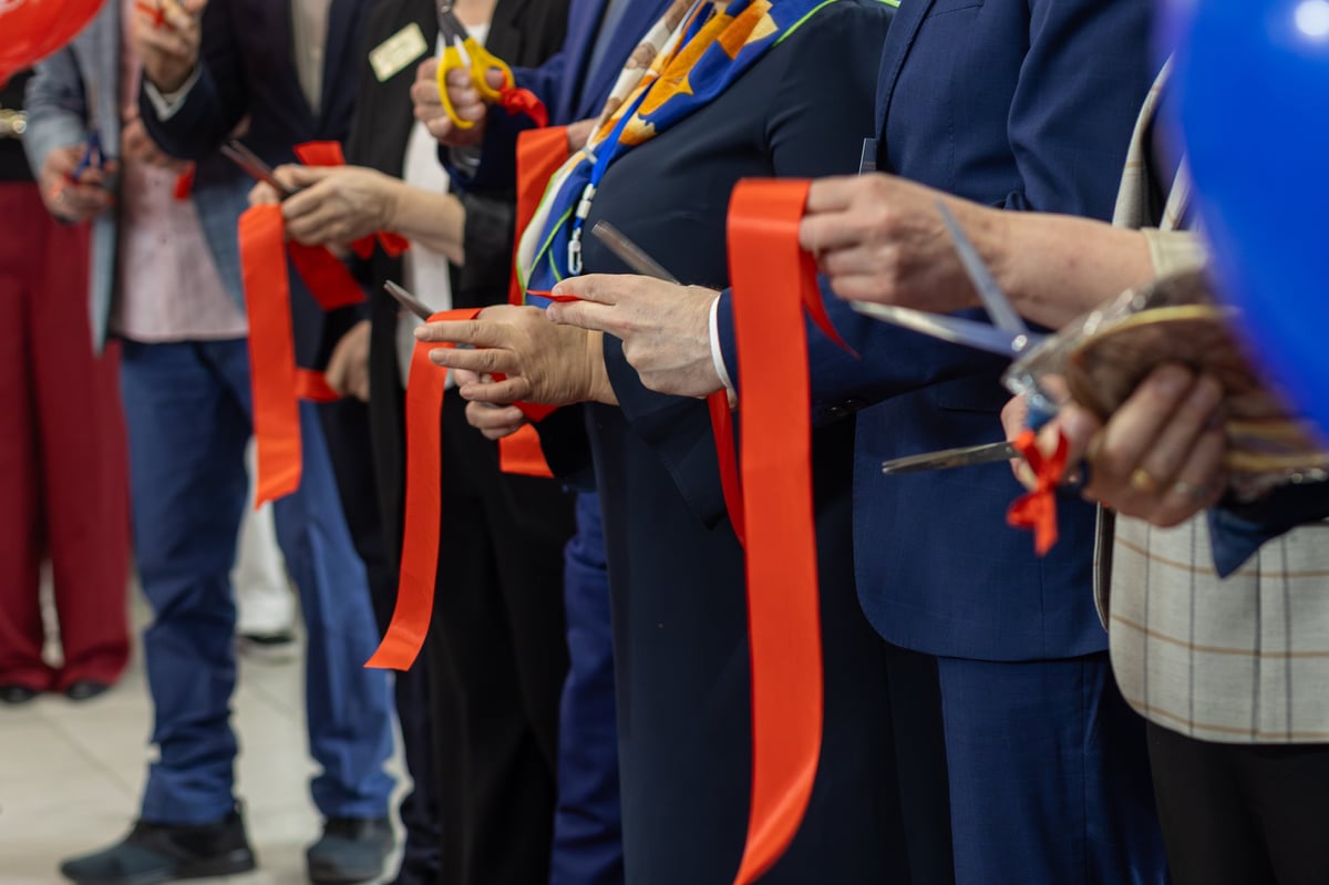 Business group cutting red opening ribbon during a formal opening ceremony